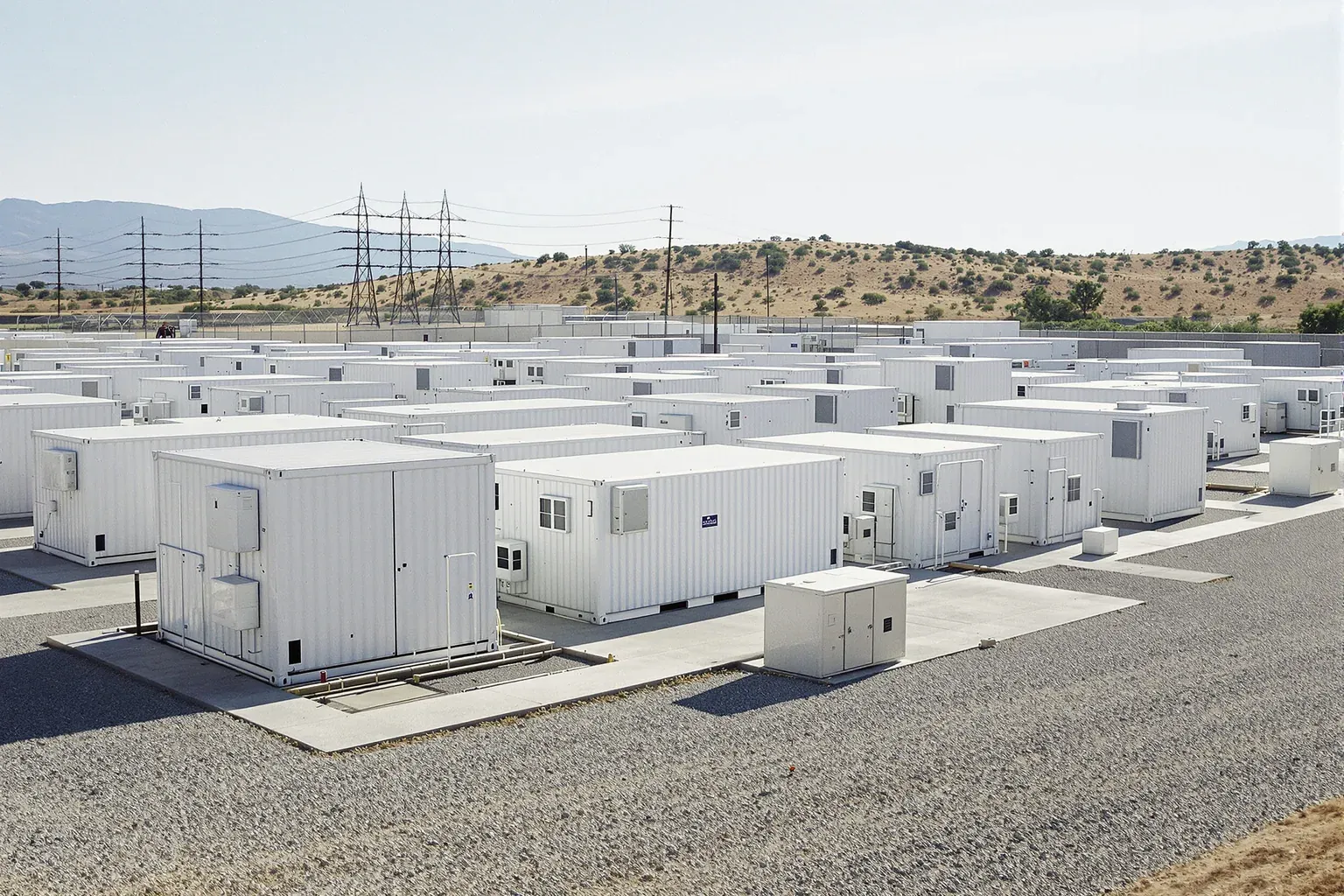 Outdoor battery energy storage system yard with rows of battery enclosure containers on concrete pads.
